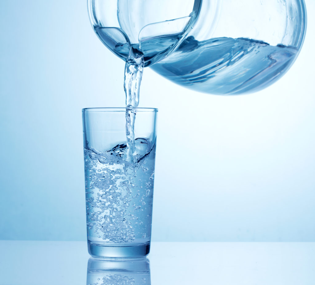 glass of water water is pouring from pitcher into glass on table